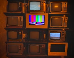 A collection of vintage televisions featuring static and color test patterns on the screens.